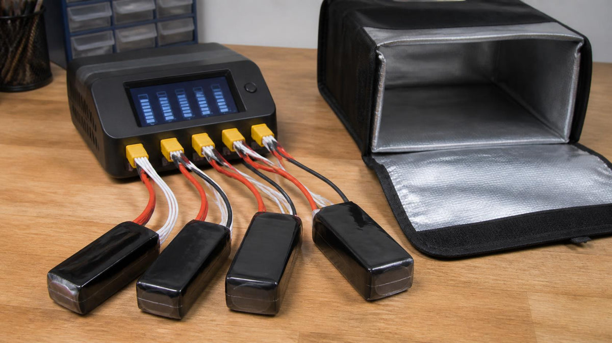 Four LiPo battery packs balance charging on a multi-port charger beside an open fireproof LiPo bag