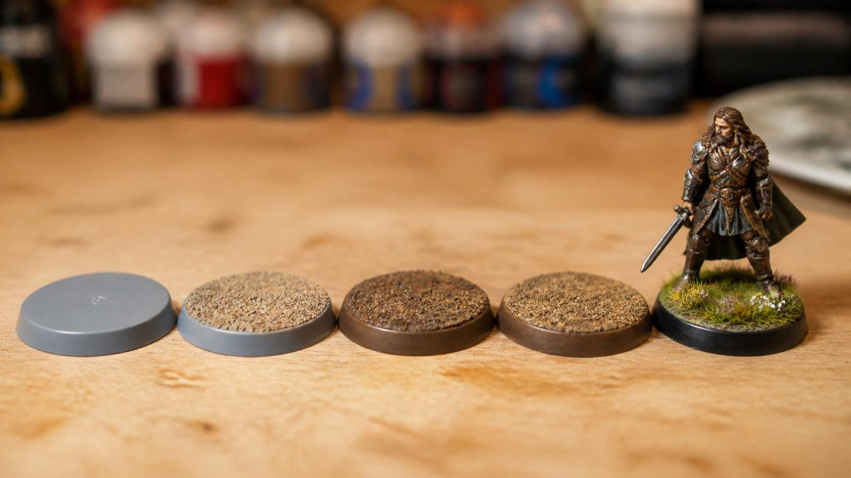 Row of miniature bases from bare plastic to sand, painted, drybrushed and finished with tufts and a black rim under a painted warrior